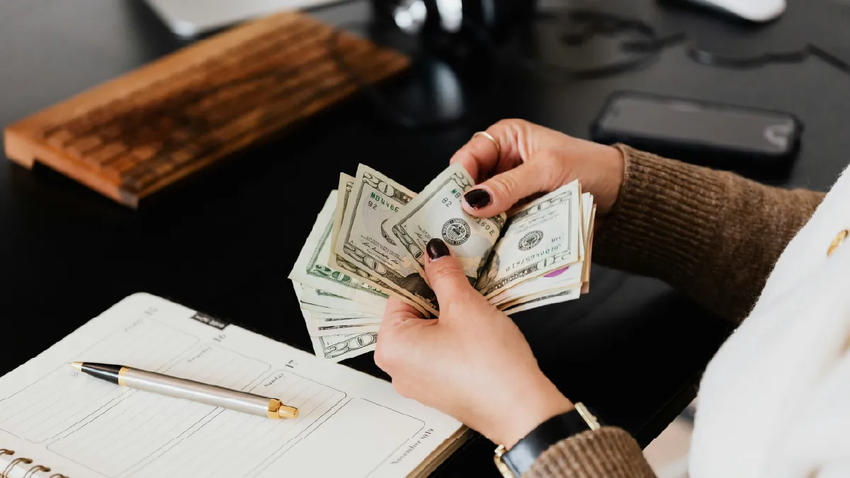 Persona contando billetes de 20 dólares sobre un escritorio con una agenda, representando el cálculo del costo de una prima de seguro de vida.