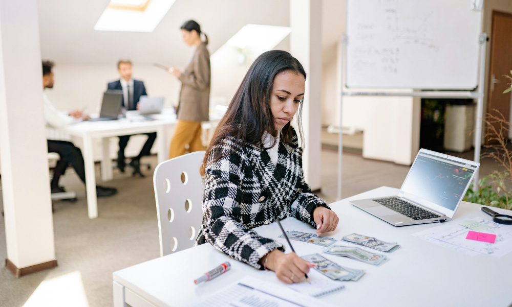 Una joven profesional en una oficina contando billetes de dólares y tomando notas para su planificación financiera.