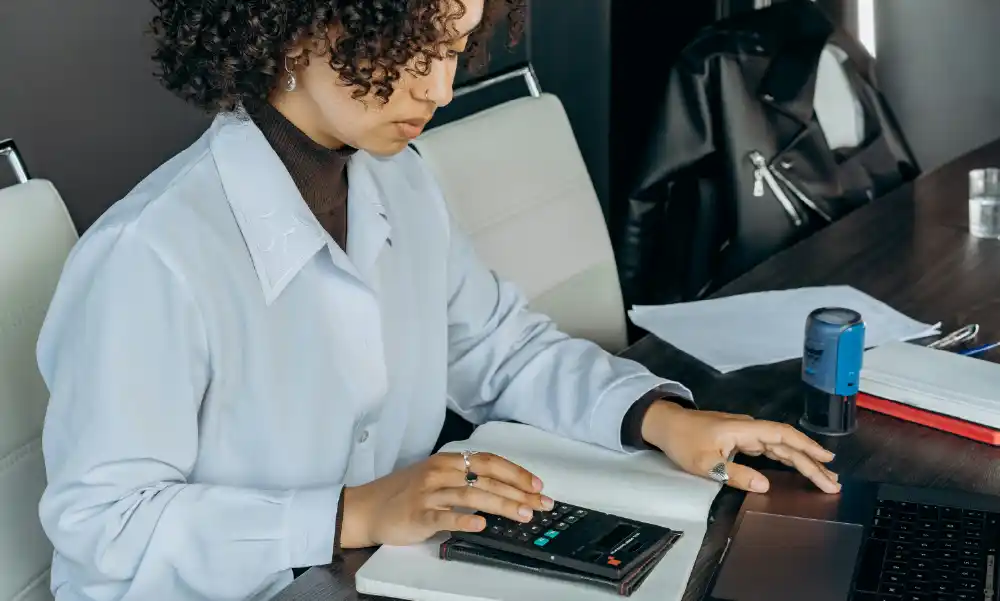 Mujer joven analizando sus finanzas personales con una calculadora y laptop para contratar un seguro de vida antes de los 30 años.