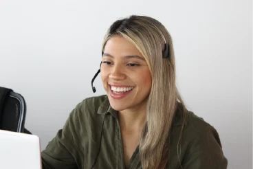 Representante de servicio al cliente sonriente con auriculares y micrófono atendiendo una llamada de soporte para una agencia de seguros.