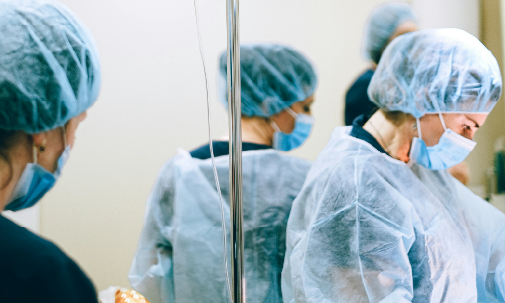 Equipo médico con batas, tapabocas y gorros quirúrgicos en un entorno hospitalario, representando la intervención médica y el respaldo de un seguro ante enfermedades de alto costo.