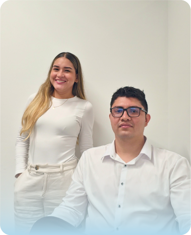 Dos especialistas del equipo de Visión Segura frente a un fondo blanco. Una mujer de cabello rubio sonríe de pie a la izquierda, vestida con una blusa blanca y pantalones beige. Un hombre con gafas está sentado a la derecha, vistiendo una camisa blanca formal.