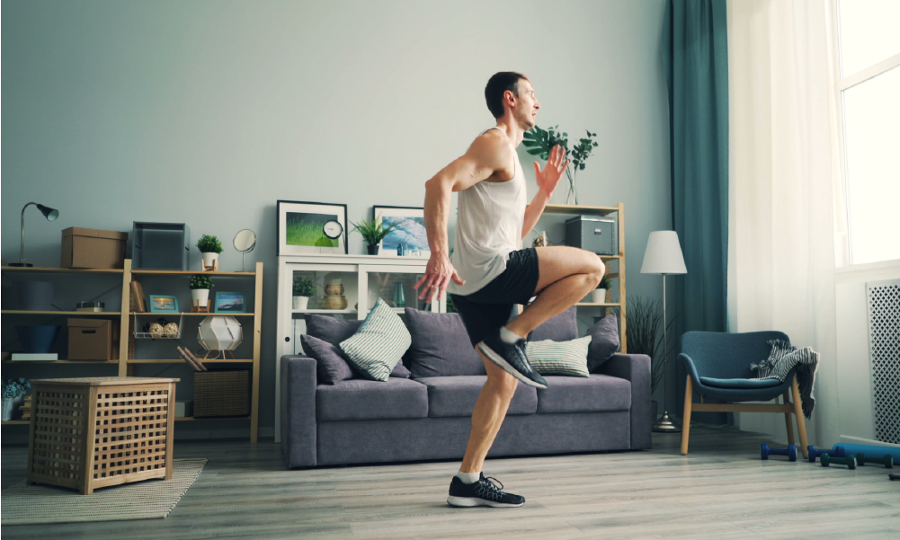 Hombre realizando ejercicio cardiovascular en su sala, elevando las rodillas para representar la energía, salud vital y protección que ofrece el Seguro de Vida SURA con su Programa Longevo.
