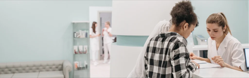 Paciente joven en la recepción de una clínica recibiendo atención del personal médico, ilustrando la cobertura de un seguro de salud en Colombia