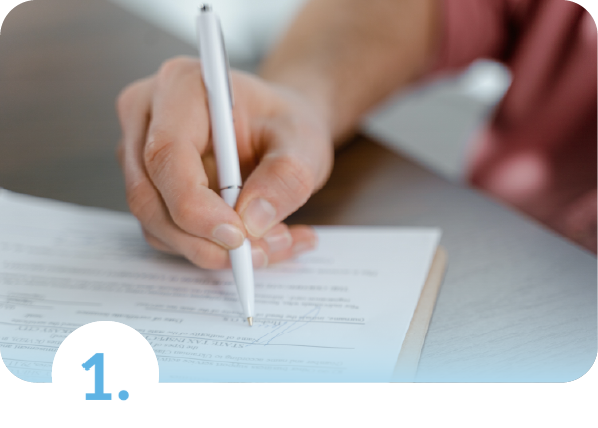 Primer plano de una mano sosteniendo un bolígrafo blanco mientras diligencia un formulario sobre un escritorio, representando el primer paso para cotizar un seguro de salud.