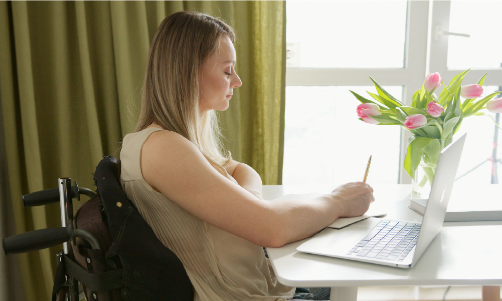 Mujer joven en silla de ruedas trabajando frente a una laptop en casa, representando la tranquilidad y protección financiera que brindan los seguros de vida y salud en Colombia