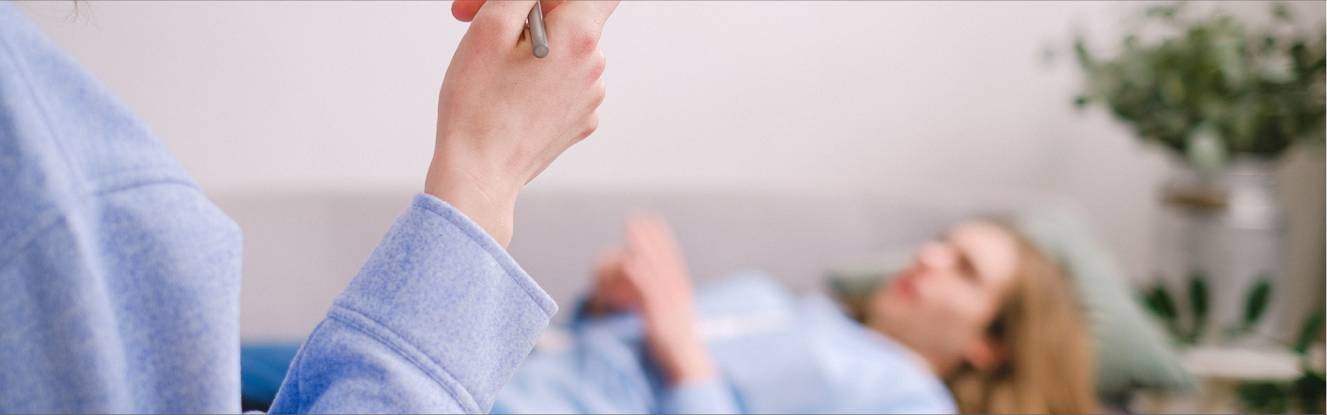 Primer plano de la mano de una psicóloga sosteniendo un bolígrafo y una tabla portapapeles, con un paciente recostado en un diván desenfocado al fondo durante una terapia.
