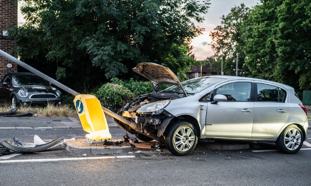 Automóvil plateado accidentado contra un poste de señalización en la vía pública, ejemplificando imprevistos y riesgos de protección personal y familiar.