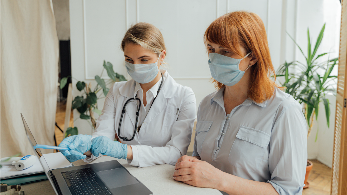 Doctora revisando en un computador opciones de cobertura médica junto a una paciente con tapabocas para elegir entre medicina prepagada, póliza de salud o plan complementario.