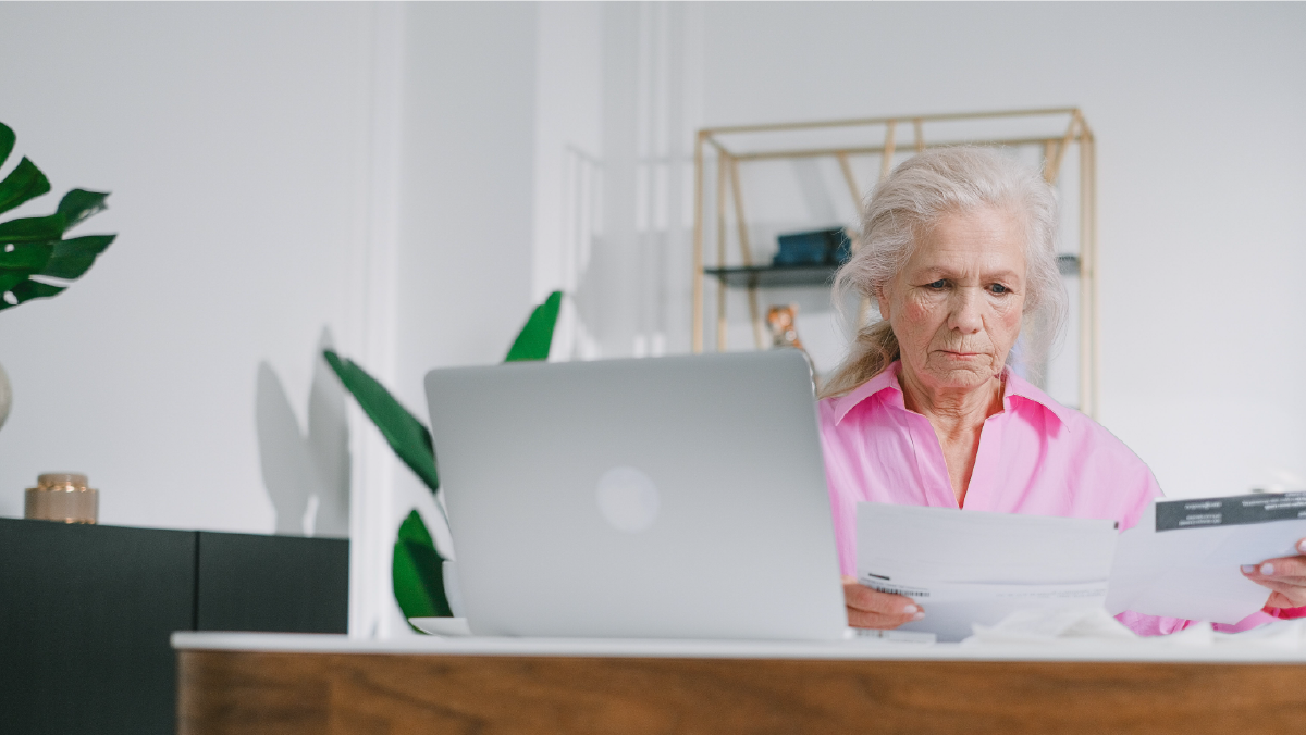 Mujer mayor revisando documentos financieros frente a una computadora portátil, representando la importancia de contar con seguro de vida y pensión en Colombia.