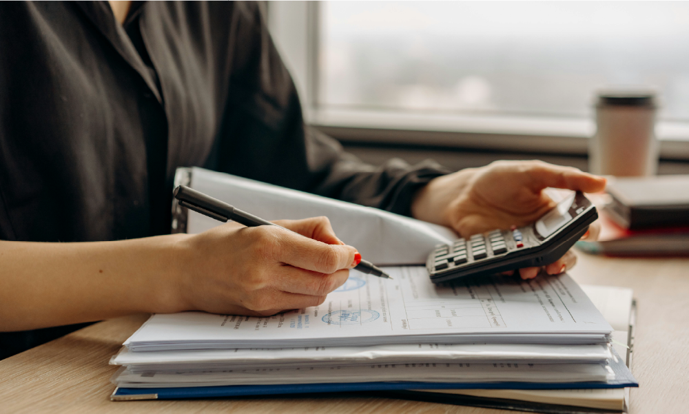 Persona calculando su brecha pensional con una calculadora y documentos financieros sobre el escritorio.